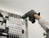 A person wearing gloves is using a flashlight to inspect an electrical panel. Podgląd zdjęcia produktu