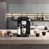 A black DeLonghi coffee machine is shown on a kitchen counter with several cups of coffee and milk in front of it. Voir les images du produit