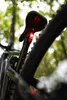 A close-up shot of a bicycle's rear light attached to the seat post, set against a blurred natural background of trees and foliage. Anteprima dell’immagine prodotto