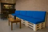 A blue pallet sofa with cushions in a cafe or lounge setting, with a small wooden table and a drink in front of it. Produktbild-Vorschau