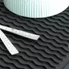 A close-up of a black dish drying mat with a wavy texture, featuring two silver utensils covered in water droplets. Náhľad obrázku produktu