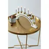 A white and gold candelabra with seven lit candles sits on a round, gold-colored table. A small white bowl filled with nuts is next to the candelabra, with a few nuts scattered on the table. Anteprima dell’immagine prodotto