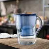 A blue and clear water filter pitcher is placed on a woven mat in a kitchen setting. Produktbild-Vorschau