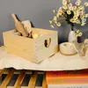 A wooden crate filled with items, placed on a surface next to a vase of flowers and a candle. Produktbild-Vorschau