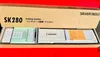 The image shows a knitting machine, the Silver Reed SK280, inside its original packaging box. The box is open, revealing the machine and some accompanying documents. Produktbild-Vorschau