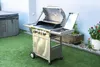 A stainless steel gas grill is shown in an outdoor setting with artificial grass and a hot tub in the background. Náhled obrázku produktu