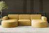 A yellow corduroy sectional sofa is shown in a room with dark paneled walls and a light gray floor. A potted plant is to the left of the sofa. Produktbild-Vorschau