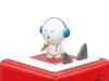 A small white figurine with blue headphones and a gold microphone stands on a red base, flanked by two gray shark fins. Produktbild-Vorschau