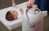 A baby lying on a changing mat next to a diaper pail. Produktbild-Vorschau