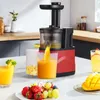A red and black juicer is shown in a kitchen setting, with juice being poured into a glass and fruit on a plate. Náhled obrázku produktu