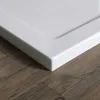 A close-up view of the corner of a white shower tray resting on a wooden floor. Produktbild-Vorschau