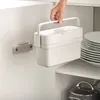 A hand is holding a white compost bin inside a kitchen cabinet, next to a stack of plates. Náhled obrázku produktu