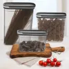 Three clear plastic food storage containers with gray lids, filled with spaghetti, pasta shells, and dried mushrooms, are arranged on a wooden cutting board and a white surface. A small bunch of cherry tomatoes is in the foreground. Náhľad obrázku produktu