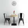 A small round bistrot table with two chairs, set against a white wall with a clock. Náhled obrázku produktu