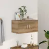 A wooden wall cabinet with two doors is mounted on a white wall. Decorative items, including a vase with greenery, a framed picture, and books, are placed on top of the cabinet. Below the cabinet, a wooden drawer unit holds more decorative items and books. Anteprima dell’immagine prodotto
