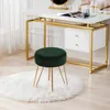 A dark green velvet stool with gold metal legs sits on a white fluffy rug in front of a white and gold vanity desk. Produktbild-Vorschau