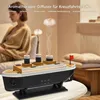 A woman is sitting in the background, out of focus, while a ship-shaped aromatherapy diffuser is in the foreground, emitting steam. Produktbild-Vorschau