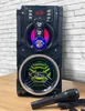 A black portable Bluetooth speaker with colorful LED lights and a microphone in front of a brick-patterned background. Produktbild-Vorschau