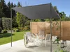 An outdoor dining set under a pergola on a wooden deck, with a garden and wooden fence in the background. Náhľad obrázku produktu