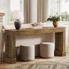 A farmhouse console table with decorative legs, placed behind a sofa, with two ottomans in front. A lamp and a vase with greenery are on the table. Podgląd zdjęcia produktu
