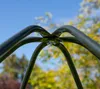 A close-up view of the top joint of a metal frame structure, likely part of a greenhouse or swing set, against a blurred background of trees and sky. Produktbild-Vorschau