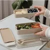 Hands holding a two-tiered lunchbox filled with food, with cutlery and a lid on a table. Podgląd zdjęcia produktu