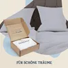 An open box with bedding inside, placed on a bed with pillows. Produktbild-Vorschau