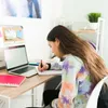 A young girl is sitting at a desk and writing in a notebook. Anteprima dell’immagine prodotto