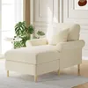 A beige chaise lounge chair with a pillow in a well-lit room with a large window and plants. Náhled obrázku produktu