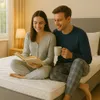 A couple sitting on a mattress in a bedroom, reading a book and drinking coffee. Produktbild-Vorschau