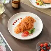 A close-up shot of a white plate with spaghetti and vegetables, set on a wooden table with other dining items. Produktbild-Vorschau