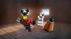 Three LEGO figures are arranged on a wooden floor with two small windows in the background showing a beach scene. Produktbild-Vorschau
