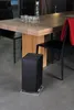 A black air purifier sits on a gray floor next to a wooden dining table with chairs. Podgląd zdjęcia produktu