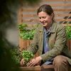 A woman is gardening and planting herbs in a wooden planter. Anteprima dell’immagine prodotto