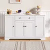 A white sideboard cabinet with a coffee maker and fruit on top, set against a paneled wall. Náhľad obrázku produktu