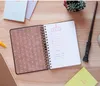 A notebook is open on a wooden desk, with a wand and other stationery items. Produktbild-Vorschau