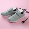 A pair of light blue sneakers with white soles and velcro straps, each with a white shoe dryer inserted into it. A black power cord and plug are visible. Produktbild-Vorschau