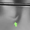 A close-up view of a dent on a stainless steel appliance, indicated by a green arrow. Produktbild-Vorschau