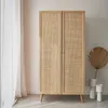 A wooden wardrobe with rattan doors stands against a light-colored wall, with sheer curtains on the left and decorative dried palm leaves and vases on the right. Produktbild-Vorschau