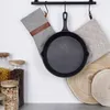 A cast iron skillet hangs on a rack with oven mitts and wooden coasters nearby, alongside jars of food items. Produktbild-Vorschau