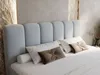 A close-up view of a bed with a light gray upholstered headboard and pillows. Produktbild-Vorschau