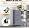 A grey kitchen cart with a wooden top, featuring drawers and shelves, is shown in a room setting. Insets highlight the wheels and their locking mechanism. Podgląd zdjęcia produktu