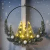 A decorative Christmas wreath with LED lights and miniature trees, hanging in front of a window with a snowy background. Anteprima dell’immagine prodotto