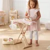 A young girl is playing with a toy ironing board and clothes in a room. Podgląd zdjęcia produktu