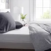 A neatly made bed with gray bedding and pillows, next to a window. Produktbild-Vorschau