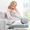 A woman is sitting on a couch with a heating pad on her lap. Produktbild-Vorschau