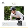 A man wearing a cycling helmet and sunglasses is riding a bicycle, with a microphone clipped to his shirt. A pair of wireless earbuds in their charging case are shown in the foreground. Anteprima dell’immagine prodotto