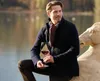 A man holding a glass of red wine, leaning against a stone sculpture near a body of water. Produktbild-Vorschau