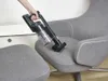 A hand holding a cordless vacuum cleaner over a gray chair. Voir les images du produit