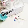 A white handheld sewing machine is displayed on a white surface, with spools of thread and other small sewing accessories scattered around it. A blurred basket with pink ribbons is in the background. Náhled obrázku produktu